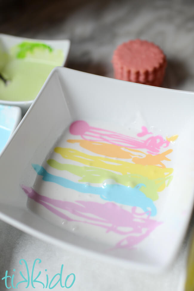 A pastel rainbow of royal icing in a white bowl for making marbleized royal icing decorated sugar cookies.