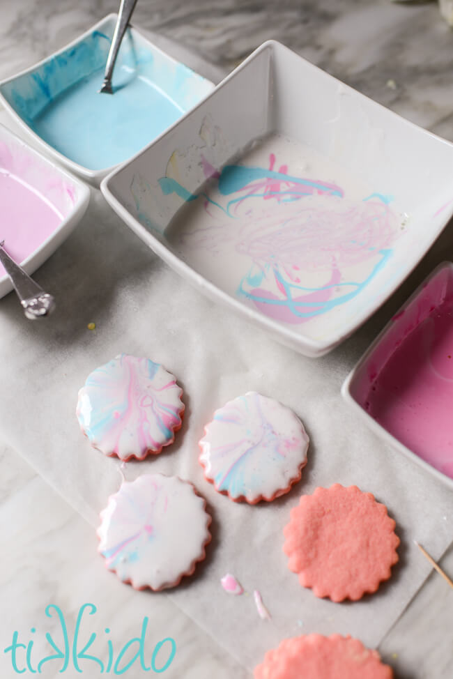 Cotton candy cookies being decorated with marbleized pink, blue, and purple royal icing.