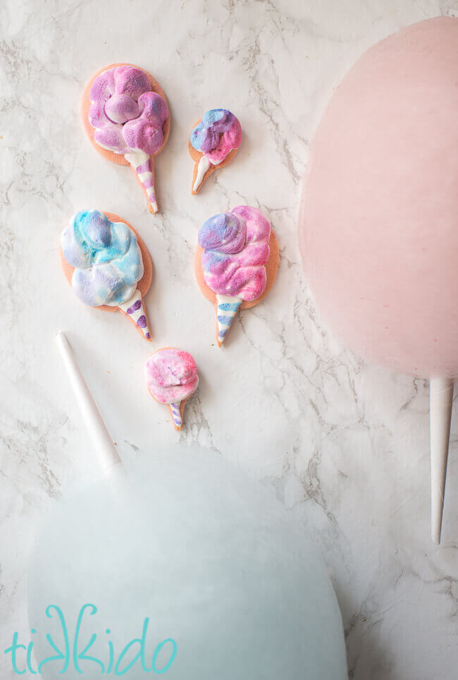 Cotton Candy Cookies decorated with royal icing, next to cones of cotton candy.