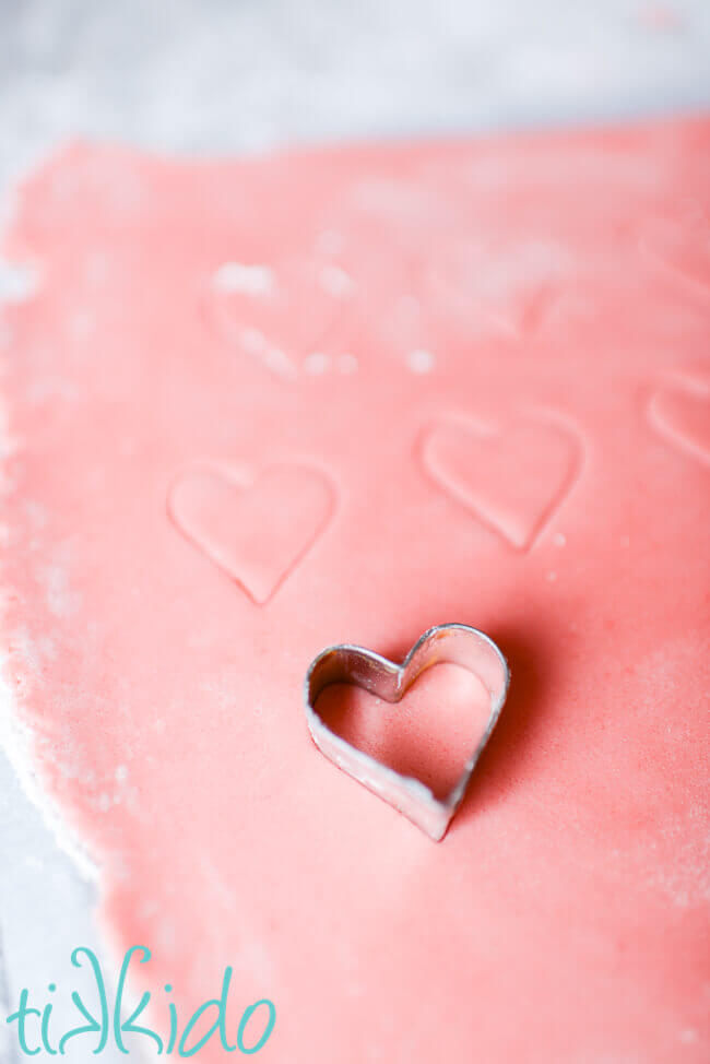 Sugar cookie dough being cut into small heart shapes to make Conversation Heart Sugar Cookies