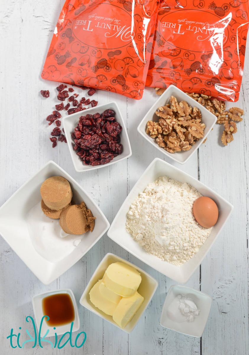 Ingredients for making Cranberry Walnut Cookies measured out in white bowls, sitting on a white wooden surface.
