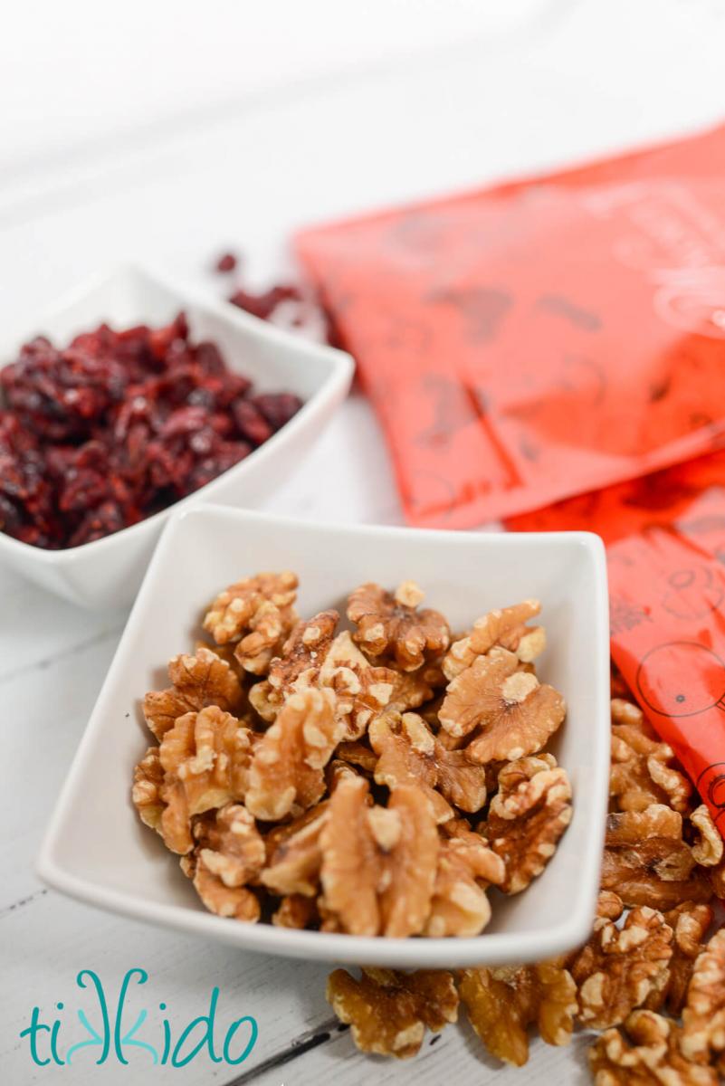 walnut halves and dried cranberries in two square, white bowls.