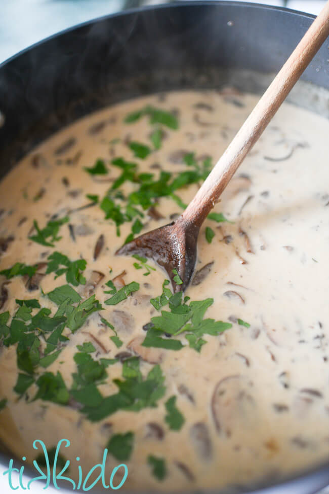 Cream and herbs being stirred into Cream of Mushroom Soup.