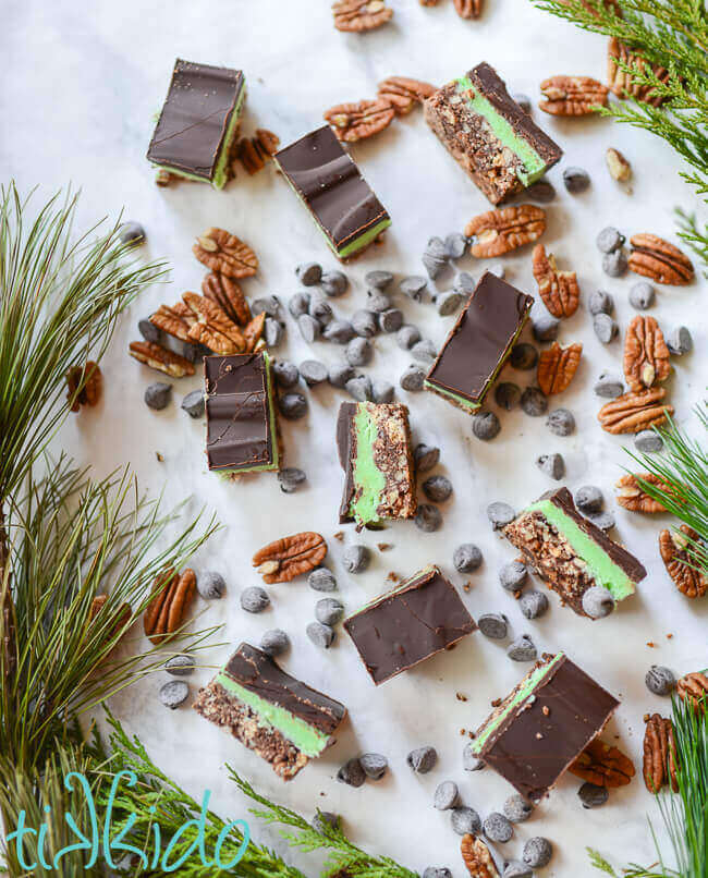 No bake creme de menthe bars surrounded by walnuts, chocolate chips, and fresh evergreen branches.