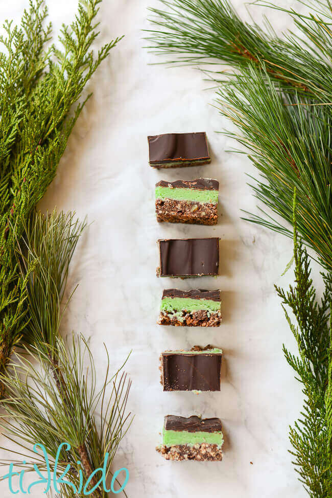 No Bake creme de menthe bars lined up on a white marble surface, surrounded by fresh evergreen branches.