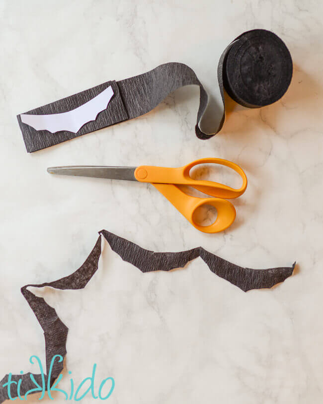 Crepe paper folded and a bat shaped template used to cut the crepe paper into a bat garland.