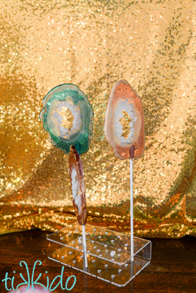 Three lollipops that look like agate slices in front of a gold sequin backdrop.