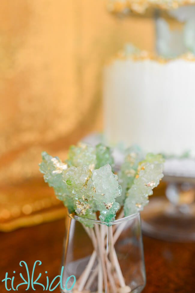 Rock candy in shades of green with gold leaf flecks, in a small glass shaped like a crystal.