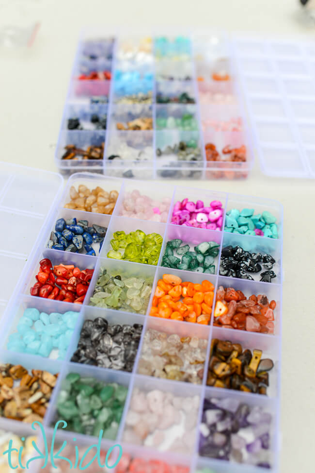 Two clear plastic boxes, each with twenty individual square compartments inside, each holding a different color of gemstone chip beads.