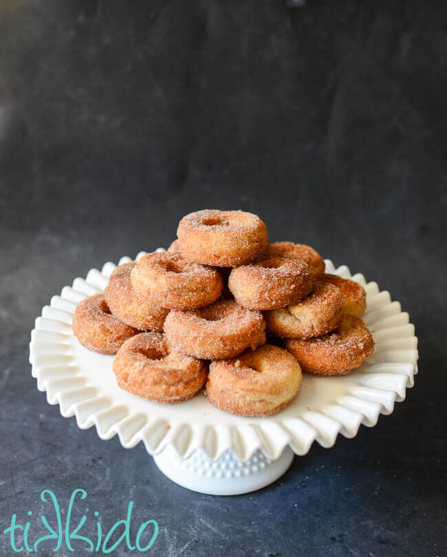 Cinnamon sugar cake donuts stacked on a white cake plate.