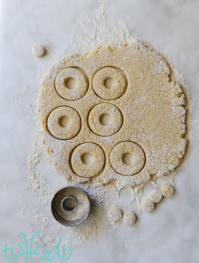 Cake doughnut dough being cut into doughnut shapes with round cookie cutters.