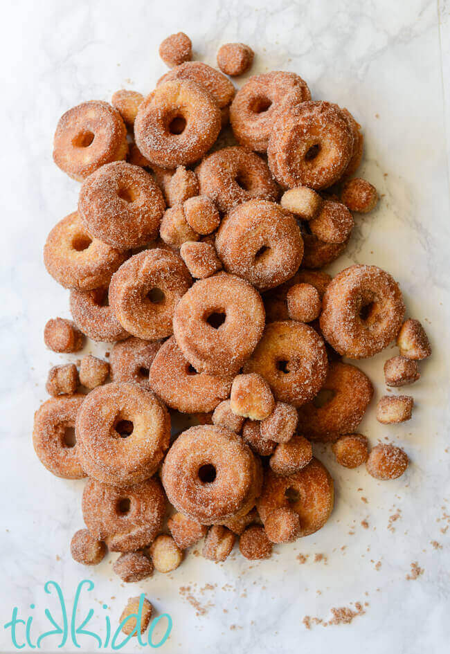 Pile of cinnamon sugar cake donuts and donut holes on a white marble background