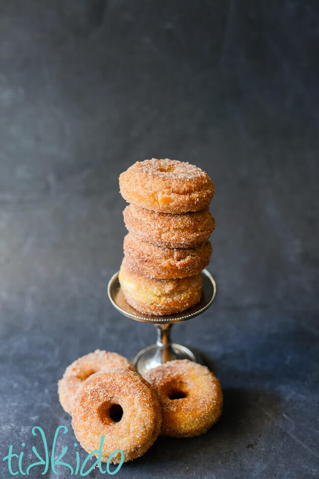Cinnamon sugar cake donuts stacked on a black chalkboard background.