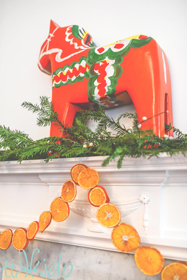 Dried orange slice garland hanging from a white fireplace mantel, below a very large dala horse.