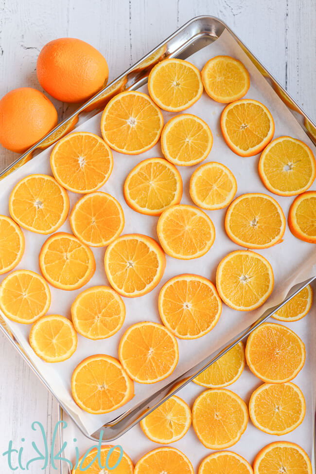 Thin slices of orange on parchment lined baking pans, ready to be dried in the oven to make Orange Garland.