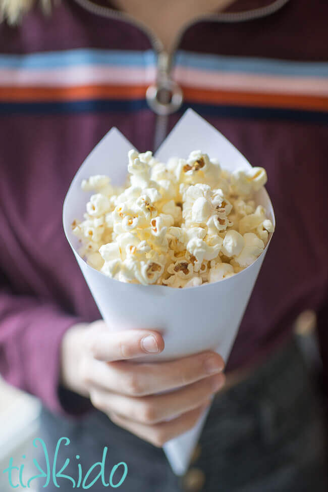 Duck fat popcorn in a white paper cone being held in a woman's hands.