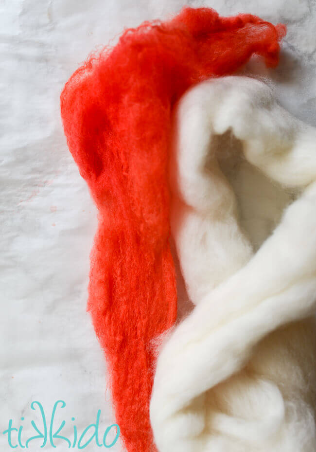 Wool roving dyed red next to natural white wool roving on a white marble background.