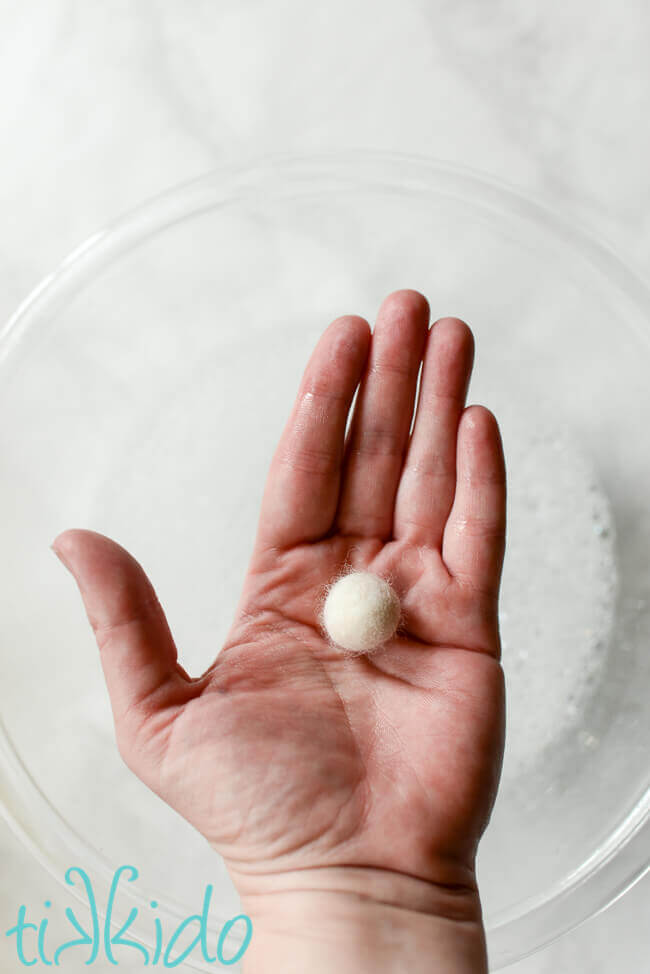 Hand holding wool felt ball above a bowl of soapy water.