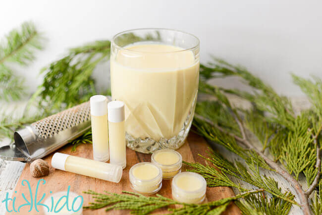 Eggnog lip balm in tubes and lip balm pots in front of a glass of eggnog and a nutmeg grater.