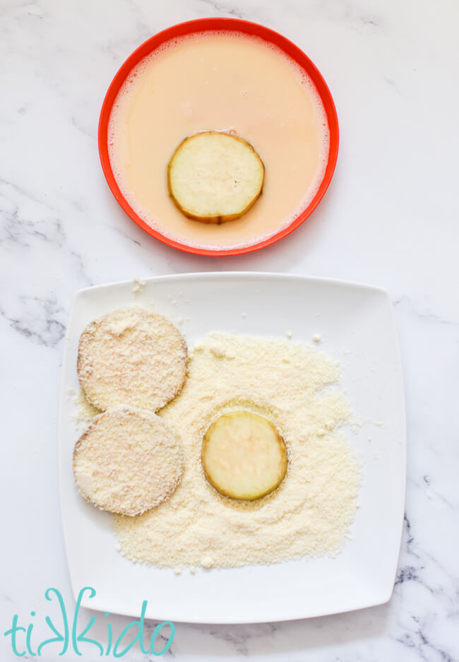 Slices of eggplant being coated in egg wash and parmesan cheese to prepare for cooking a Healthy Eggplant Parmesan Recipe.