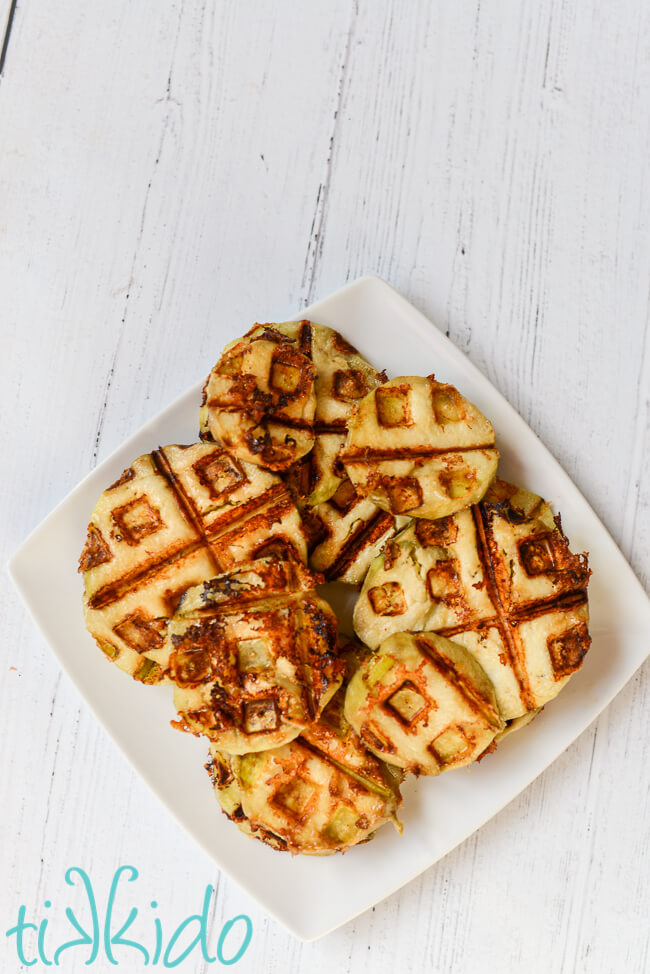 Slices of healthy eggplant parmesan made in a waffle iron on a square white plate, on a white wooden surface.