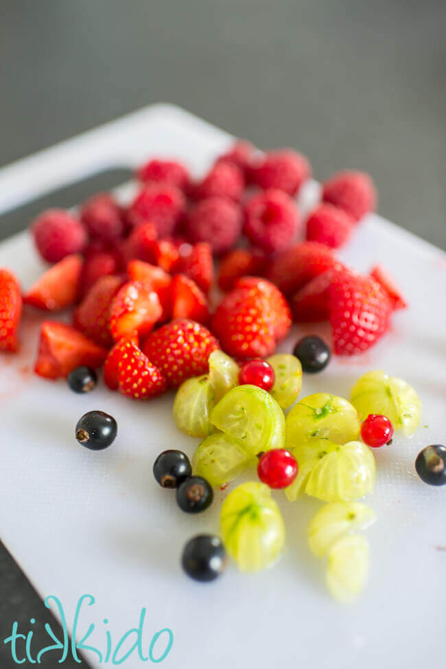 Gooseberries, currants, strawberries, and raspberries on a white cutting board.