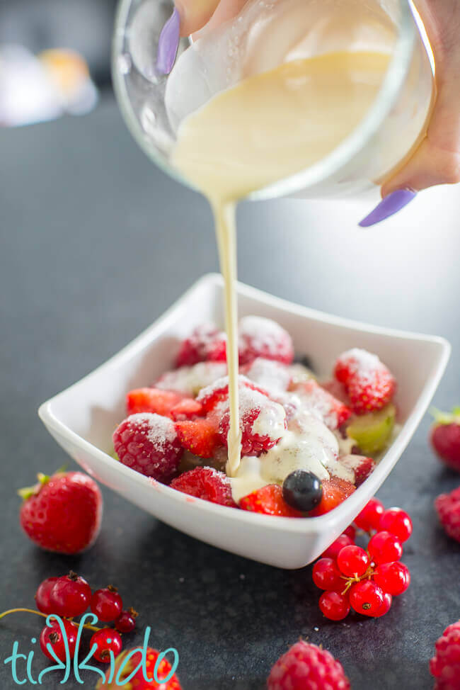 Cream pouring on a bowl full of fresh summer berries sprinkled with sugar.