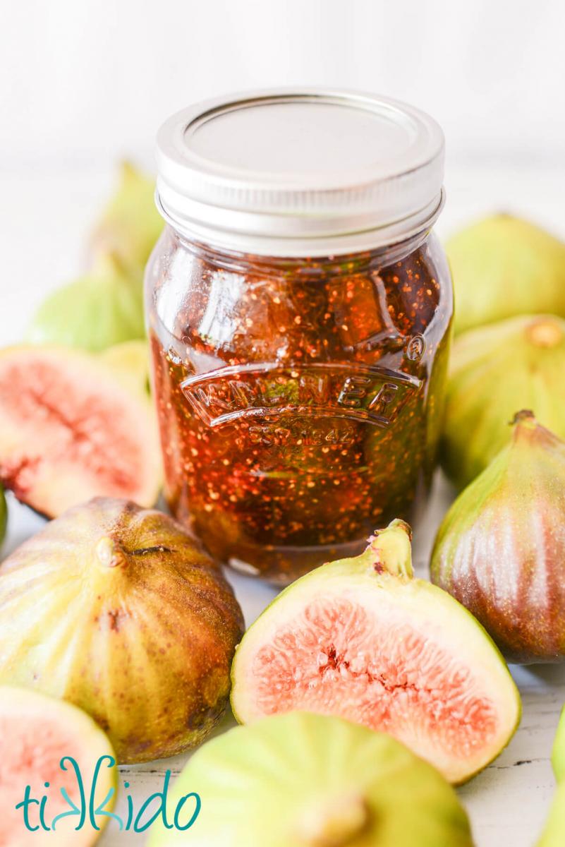 Jar of homemade fig jam surrounded by fresh figs, both whole and cut in half.