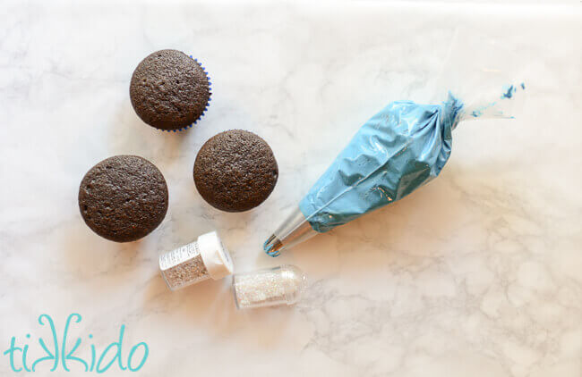 unfrosted chocolate cupcakes and a bag of blue icing