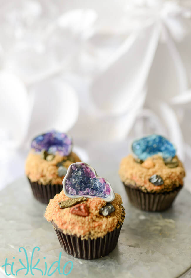 Three cupcakes with edible gum paste and sugar crystal geode cupcake toppers on a galvanized metal cake stand.