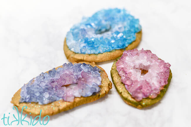 Three geode sugar cookies made from rock sugar crystals painted with food coloring, one blue and two purple.