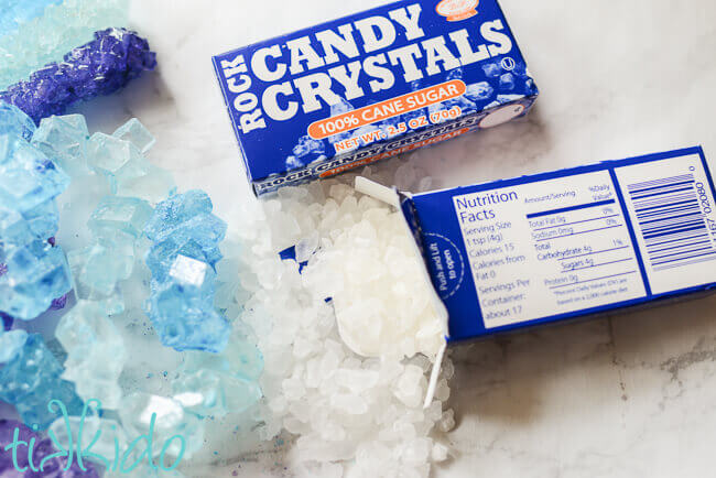 Blue, purple, and clear rock crystal sugar candies on a white marble surface.