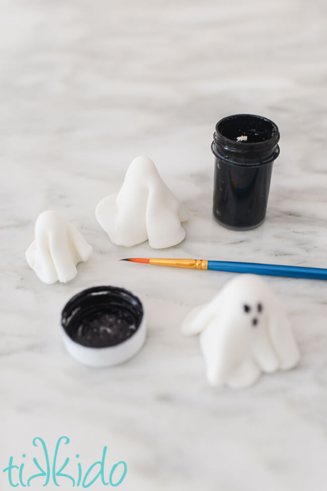 Face for the ghost cupcake toppers being painted on the ghost shape with black food coloring.