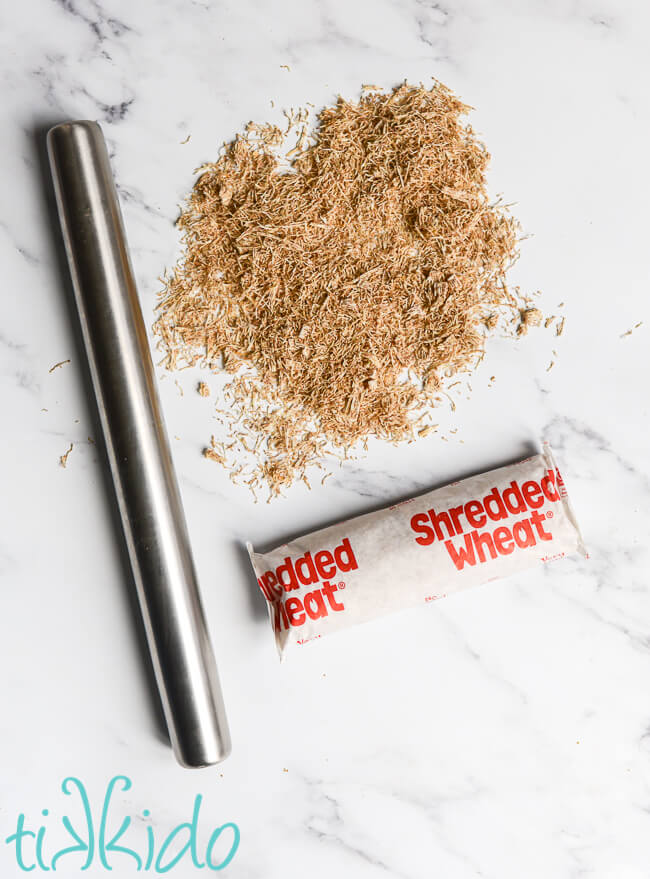 Silver rolling pin next to a pile of crushed shredded wheat to make hay and straw for the gingerbread nativity scene.