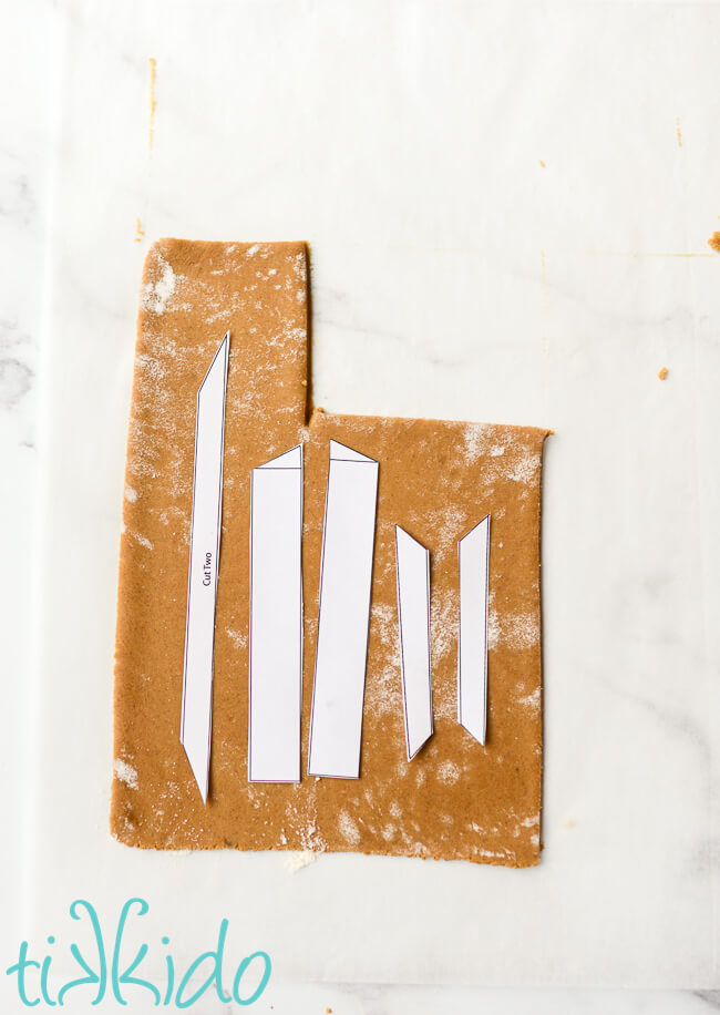 Gingerbread nativity templates on a section of rolled out gingerbread dough on parchment paper.