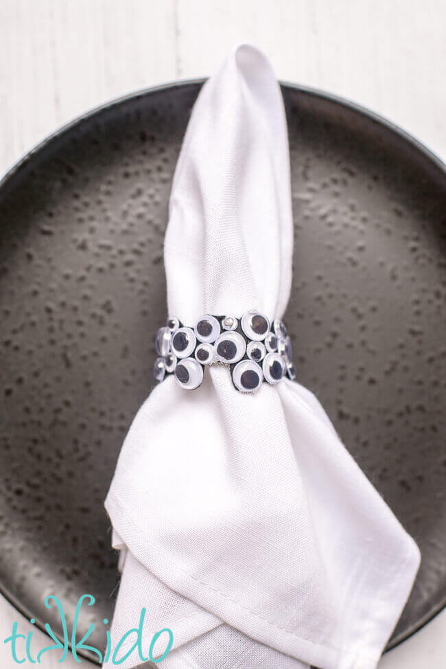 Googly eyes DIY napkin ring for Halloween on a white napkin and a black plate.