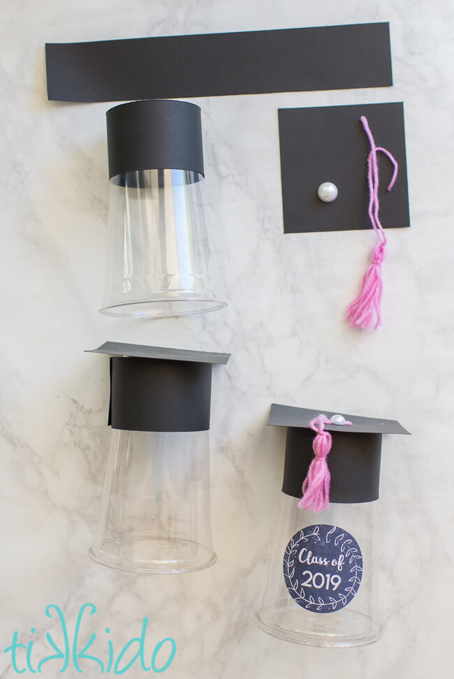 Plastic cups, paper, and yarn tassels being assembled into fillable Graduation Favors