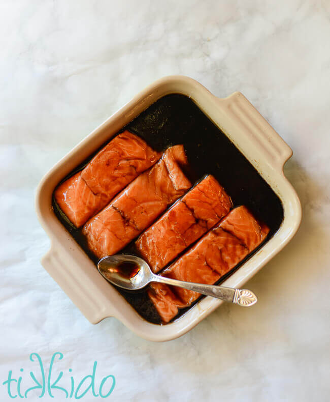 salmon marinating in marinade in a square le creuset baking dish.