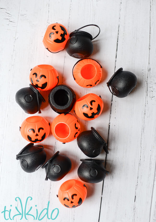 Miniature plastic pumpkins and witch cauldrons on a white wooden surface.