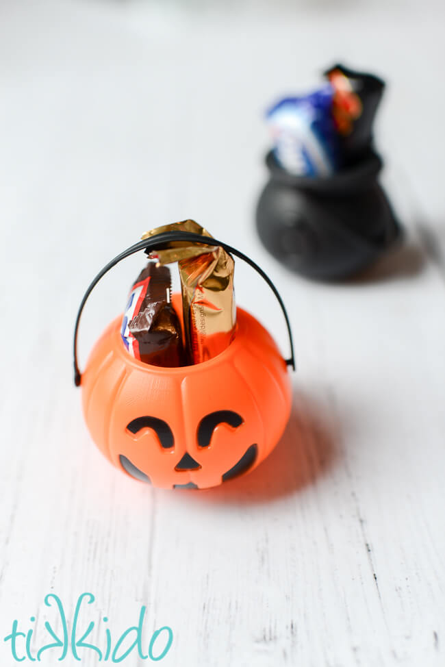 Plastic pumpkin and black cauldron Halloween favor containers filled with Halloween candy.