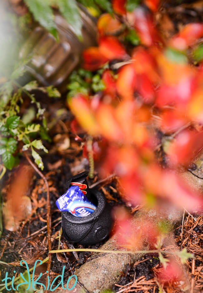 Small plastic cauldron halloween favor full of Halloween candy hidden in the yard for a Halloween candy hunt.