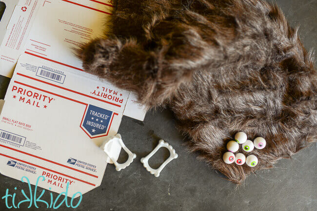 Cardboard box, fake fur, eyeball erasers, and vampire teeth on a black chalkboard background.