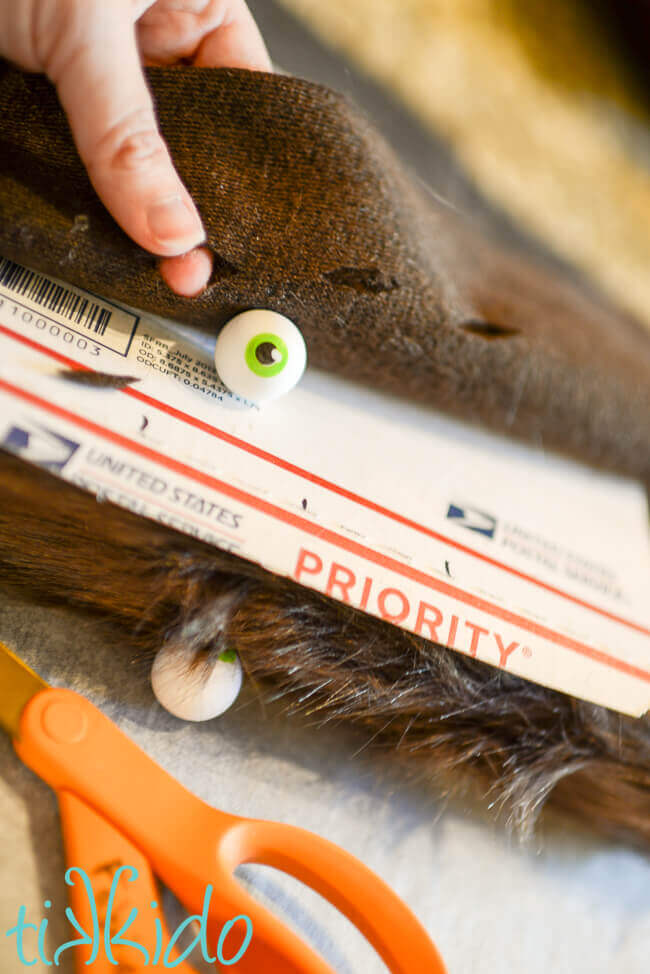 Holes in fake brown fur being cut for the eyeball erasers on the Monster Book of Monsters Box.