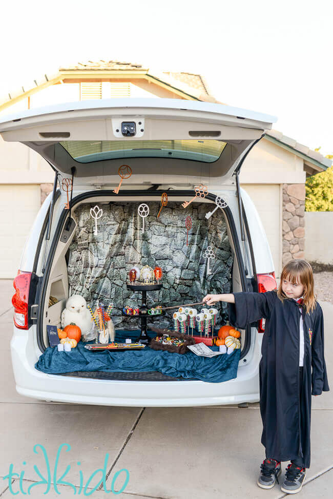 Girl dressed as Harry potter in front of Harry Potter flying keys decorating a car for a Harry potter trunk or treat.