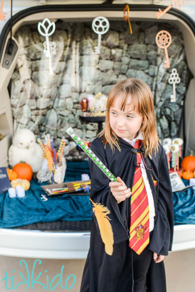 Child holding candy wand filled with green and silver Slytherin colors candies, with a feather appearing to levitate in front of the wand.