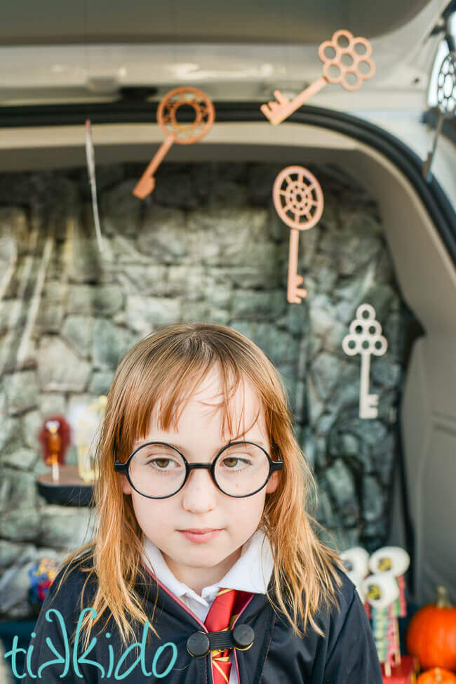Girl dressed as Harry potter in front of Harry Potter flying keys decorating a car for a Harry potter trunk or treat.