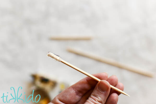 Hand holding a broken bamboo skewer with hot glue covering the broken end of the skewer.