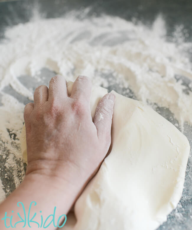 Hand kneading homemade fondant on a powdered sugar covered work surface.