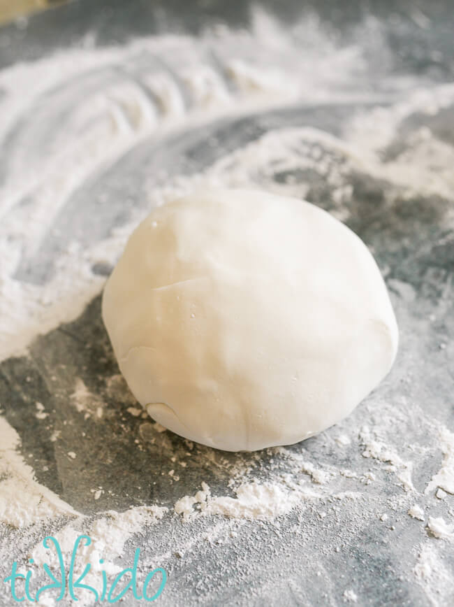 Smooth ball of homemade fondant on an icing sugar covered work surface.