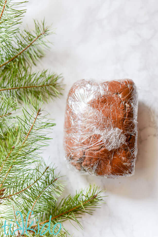 chocolate cut out cookie dough wrapped in saran wrap next to fresh pine branches.